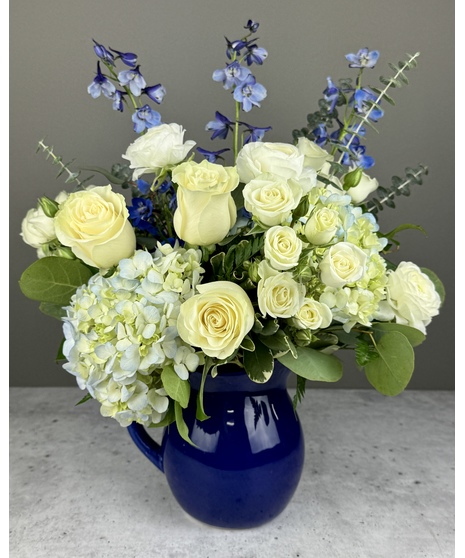 Blue and white flower arrangement with hydrangea and roses in a blue pitcher.