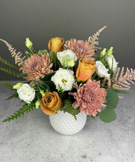 Boho arrangement with protea, roses, lisianthus, and textured blooms in blush, gold, ivory, and mauve tones.