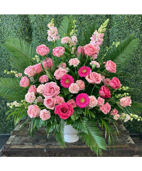 Pink floral urn arrangement with roses and seasonal blooms in a classic container. Soft, feminine tribute.