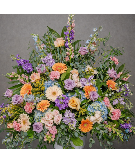 Pastel urn arrangement with pink, lavender, white blooms, and greens.