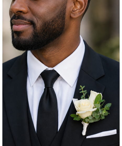 Boutonniere with blush mini roses, greenery, and delicate accents.