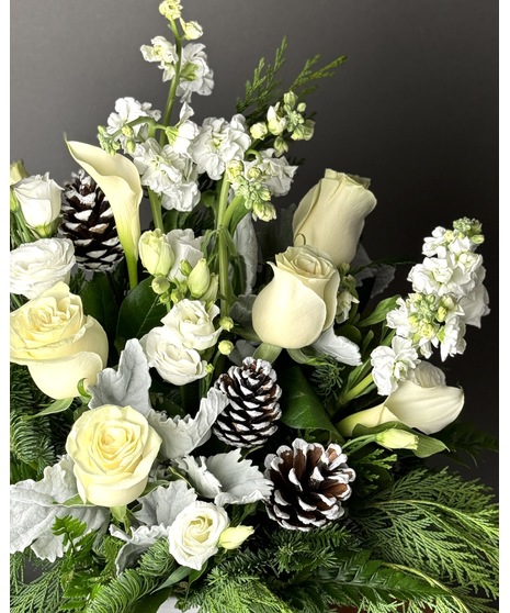 An all-white winter floral arrangement with roses, pinecones, and seasonal greens.