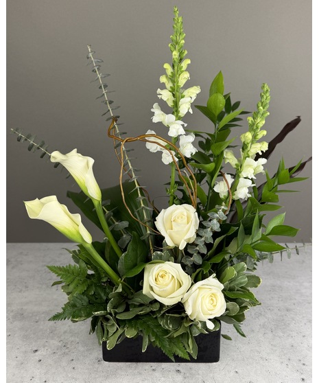 Tall white calla lilies with white roses, greenery, and ferns in a wooden container.