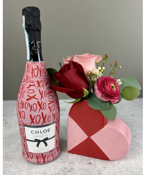 Small floral arrangement in a red and pink heart-shaped ceramic vase with romantic seasonal blooms.