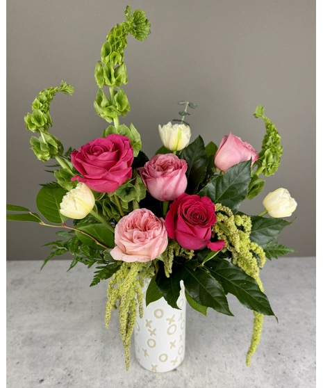 A designer's choice floral arrangement in a white ceramic vase with gold XOXO patterns. Features a mix of colorful seasonal blooms perfect for romantic occasions.