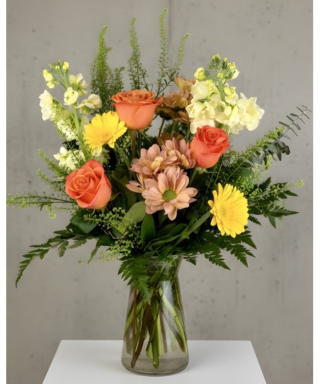 Bright arrangement of warm yellow, orange, and peach blooms in a sunny, cheerful designer’s choice style.