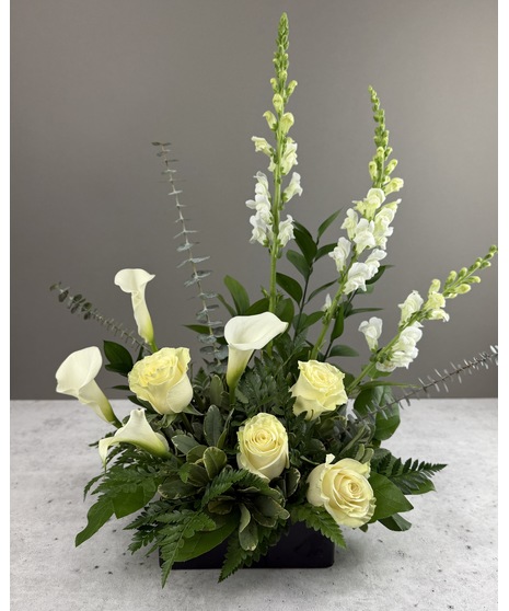 Tall white calla lilies with white roses, greenery, and ferns in a wooden container.