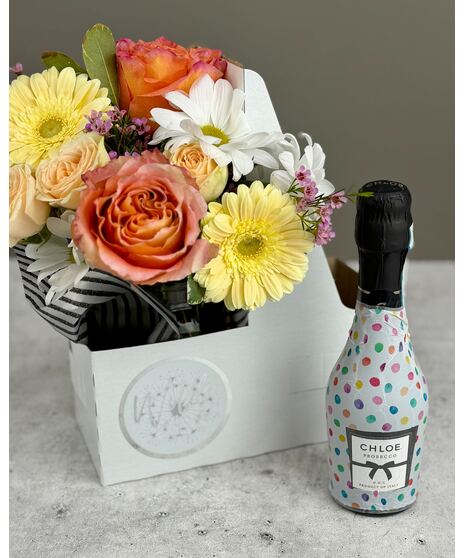Colorful flower arrangement with a bottle of Prosecco or Champagne in a gift caddy.