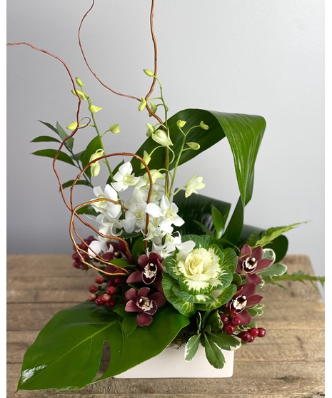 A striking arrangement featuring purple orchids, tropical greenery, and monstera leaves, presented in a sleek black vessel.
