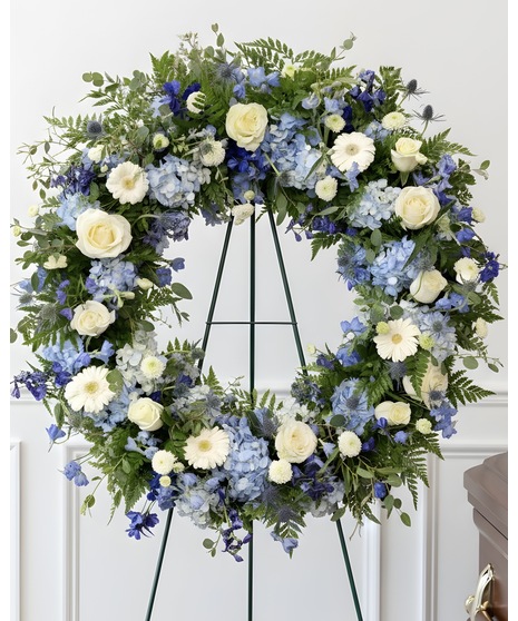 Blue, white, and green floral circle wreath displayed on an easel. Seasonal flowers used.