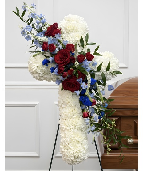 Standing cross of white roses with red roses and blue delphinium on easel.