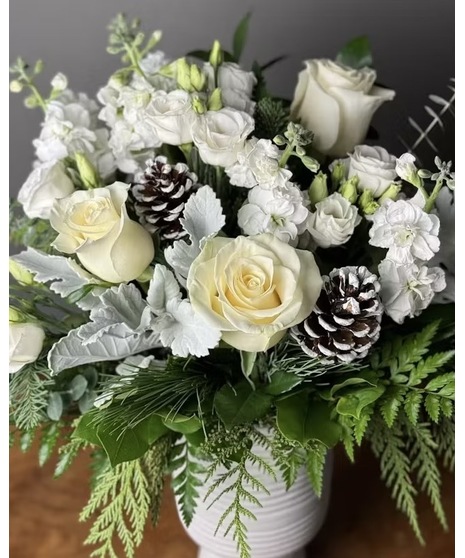An all-white winter floral arrangement with roses, pinecones, and seasonal greens.
