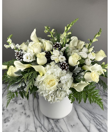 An all-white winter floral arrangement with roses, pinecones, and seasonal greens.