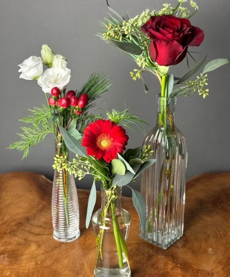 Red, white, and green Christmas arrangement with roses, daisies, berries, and pinecones.