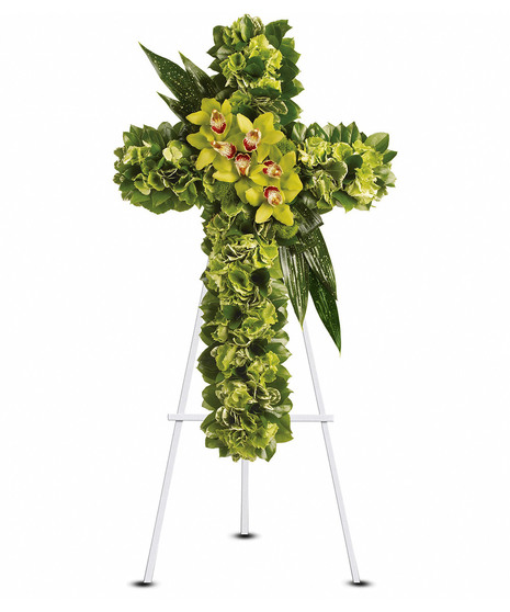 A cross-shaped sympathy arrangement of subtle green and organic-looking blooms with abundant greenery, displayed on a standing easel, symbolizing faith, peace, and renewal.
