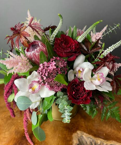 Bold red and pink floral arrangement with blooms like roses, orchids, protea and textured greenery.