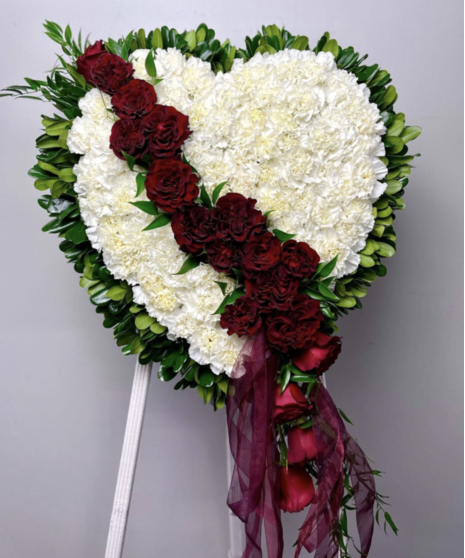 A heart-shaped sympathy wreath of rich red flowers with green accents, displayed on a standing easel, symbolizing eternal love and remembrance.