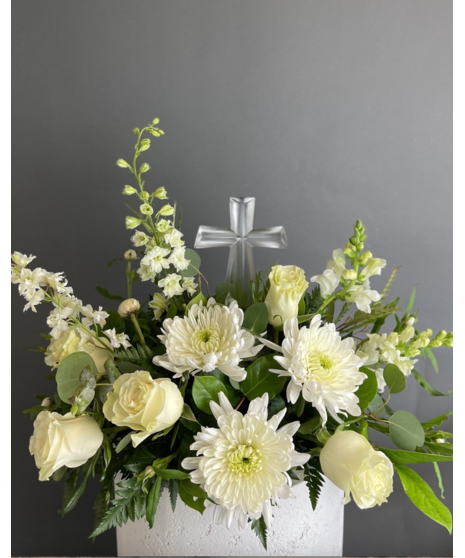 White flowers arranged around a religious keepsake like an angel, crystal cross, or ceramic heart. Four sizes available.