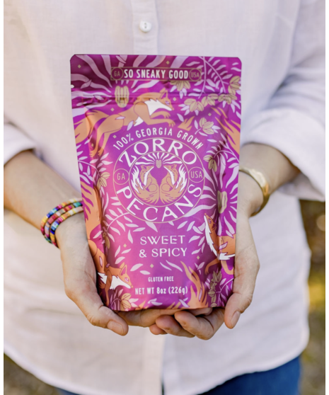 A patterned pouch of Zorro Sweet & Spicy Pecans beside a bowl filled with sugar-coated pecans.