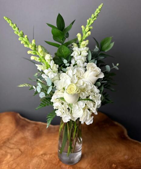 A designer’s choice arrangement featuring all white seasonal flowers in a vase, evoking peace and comfort.