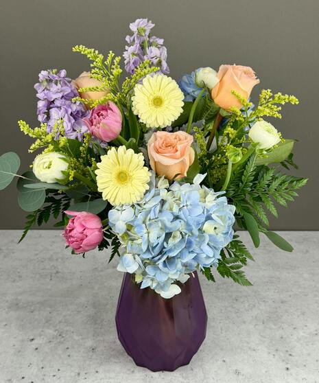 Pastel spring flower arrangement with roses, tulips, and seasonal blooms in a garden style.