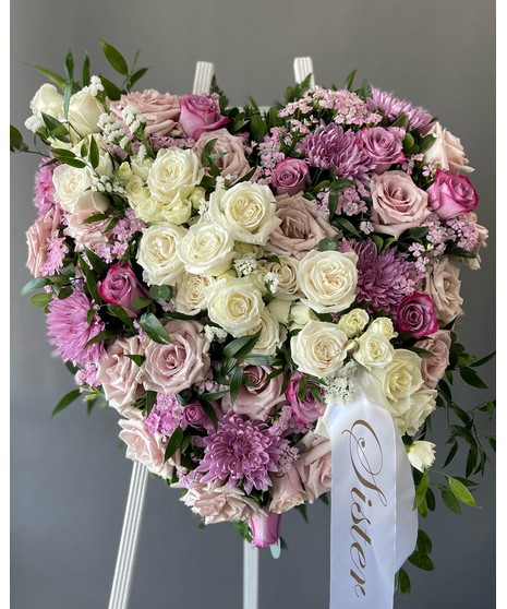 A heart-shaped sympathy wreath of pink and purple flowers with green accents, displayed on a standing easel, symbolizing love, tenderness, and remembrance.