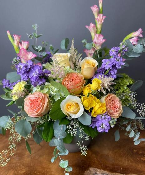 Pastel sympathy arrangement with peach roses, lavender blooms, yellow accents, and green hydrangea.
