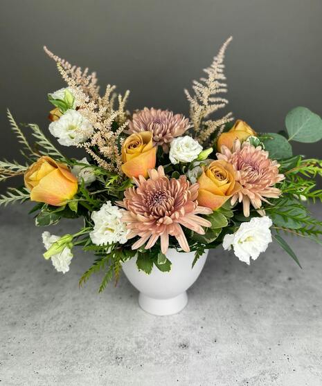 Boho arrangement with protea, roses, lisianthus, and textured blooms in blush, gold, ivory, and mauve tones.