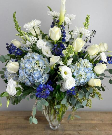 Blue and white floral arrangement with accent greenery in a glass or ceramic vase.