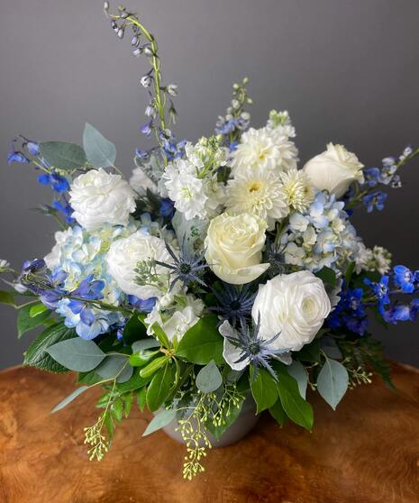 Blue and white floral arrangement with accent greenery in a glass or ceramic vase.