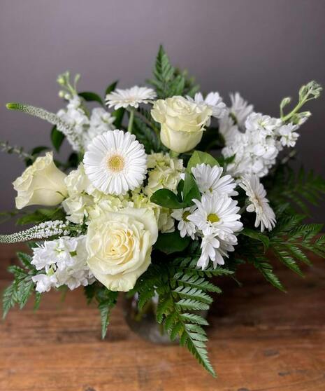 A designer’s choice arrangement featuring all white seasonal flowers in a vase, evoking peace and comfort.
