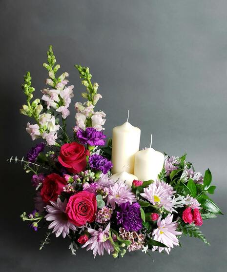 Pink and purple flowers arranged to surround an urn or photo; design based on keepsake size and shape.