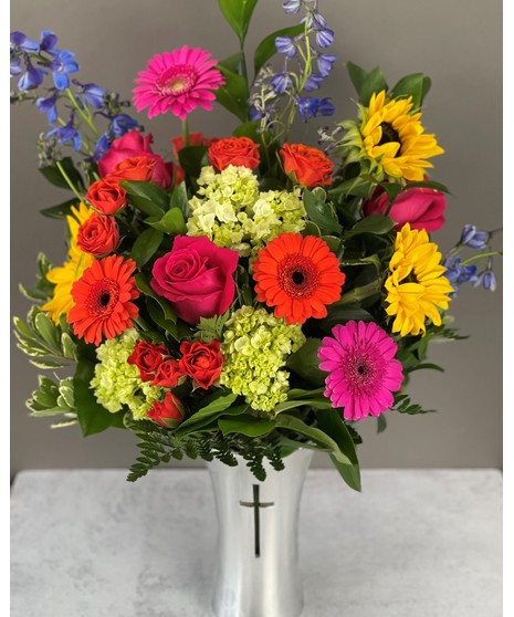A vibrant sympathy arrangement of colorful flowers in a shiny silver cross keepsake vase, available in three sizes, symbolizing hope, love, and remembrance.