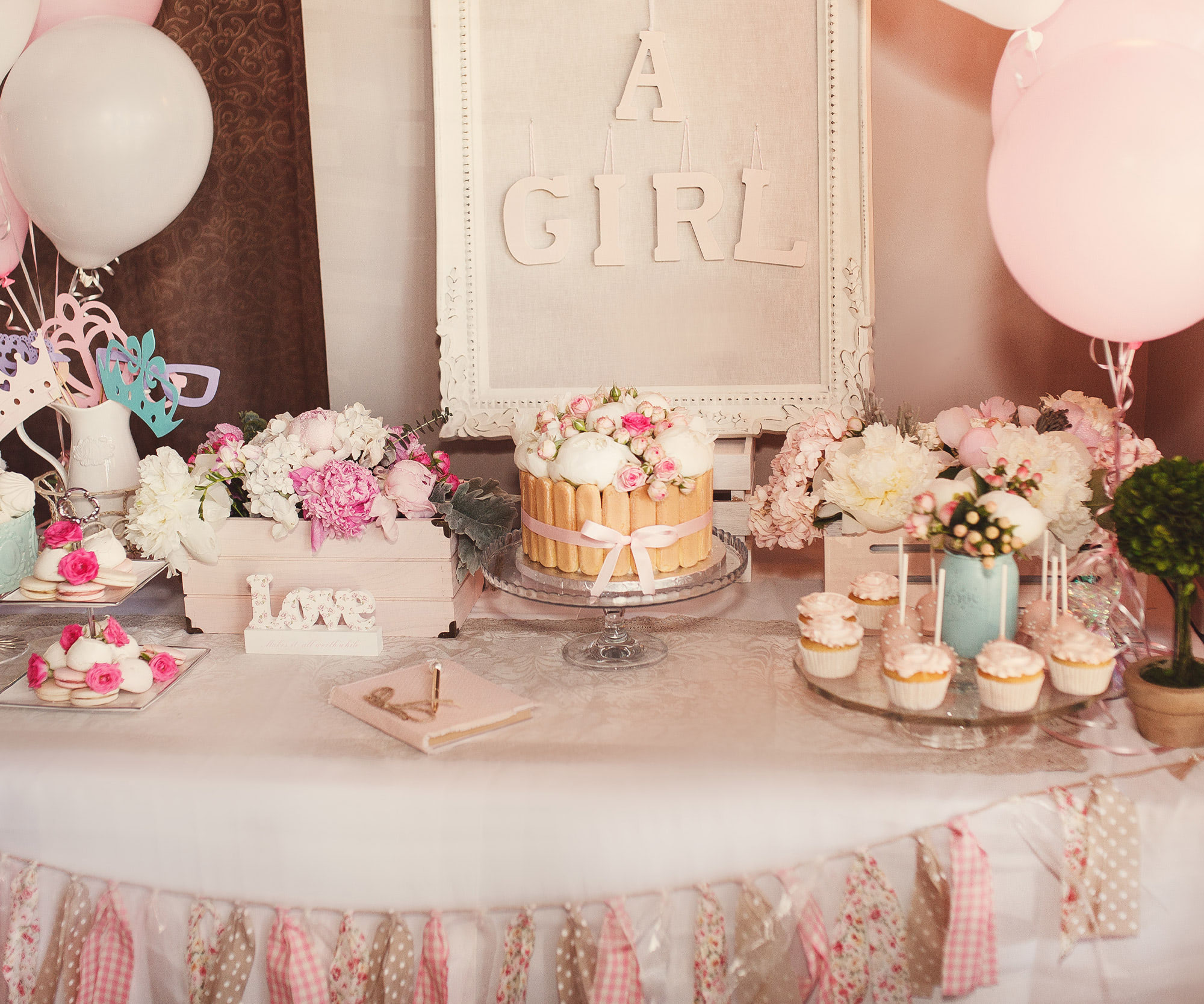 Pink baby shower dessert table with cake, cupcakes, balloons, and elegant party decorations