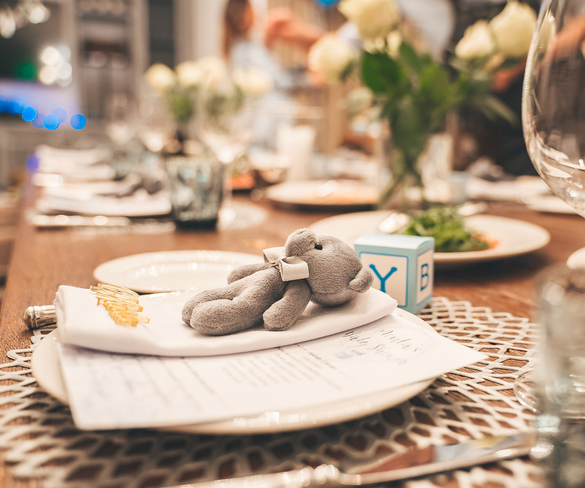 Baby shower place setting with plush elephant, baby block, and floral centerpiece on table