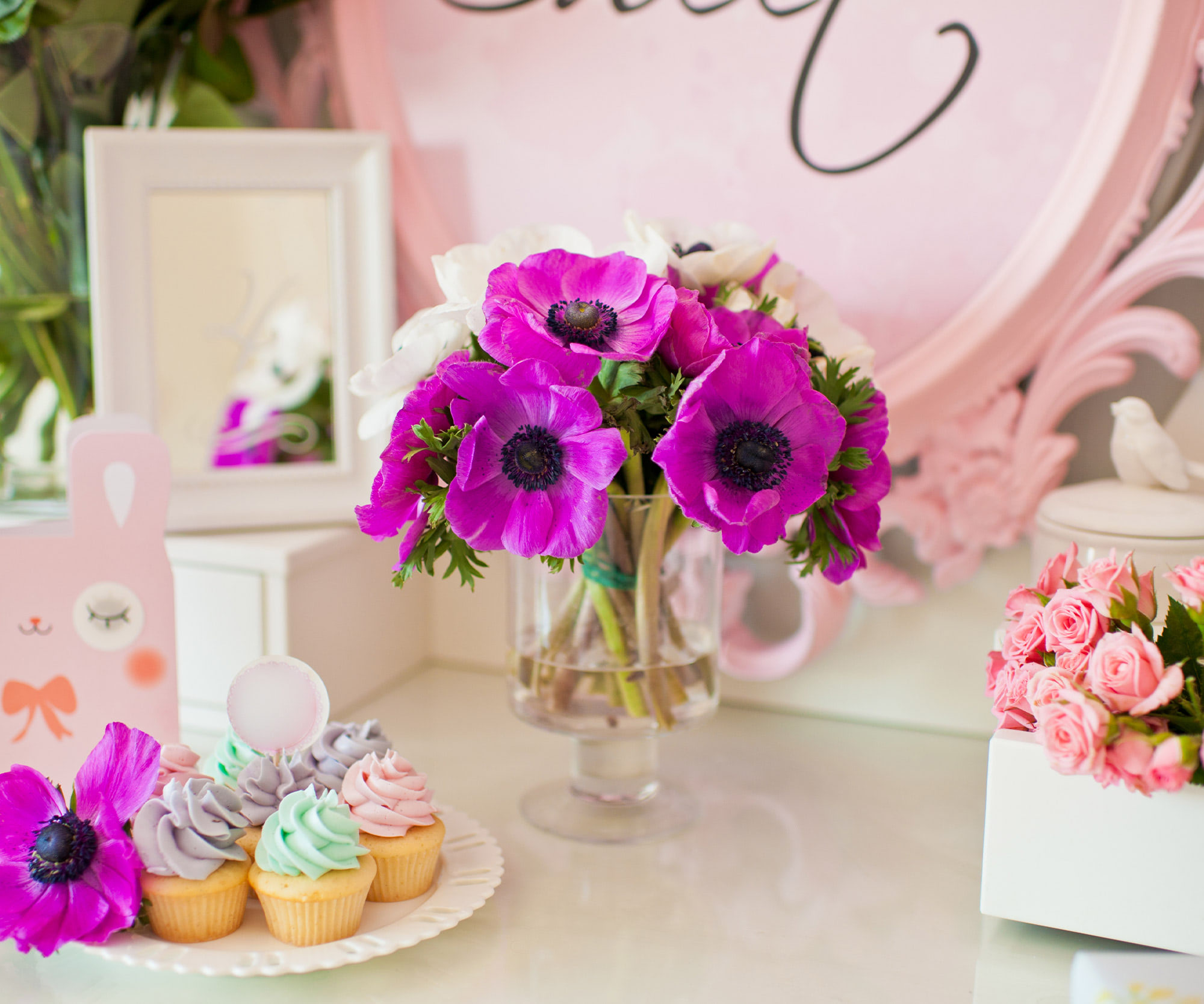 Baby shower dessert display with purple anemones, cupcakes, and pink floral party decor